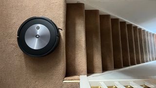 The iRobot Roomba J7+ cleaning carpet next to a set of stairs