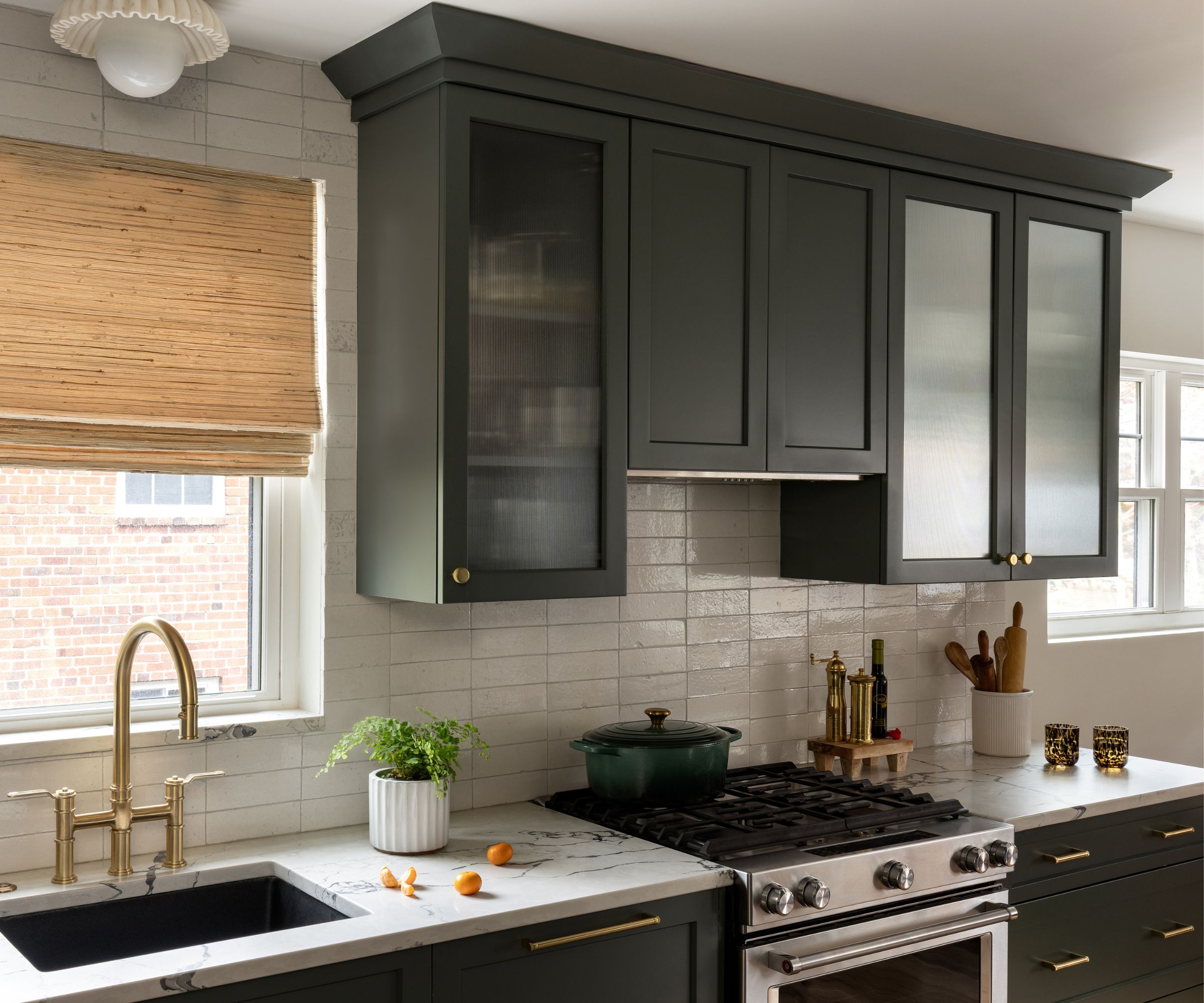 A kitchen with white walls, dark green cabinets and glass fronted upper cabinet doors