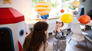 A Kid wearing an astronaut costume is looking at model planets with a parent.
