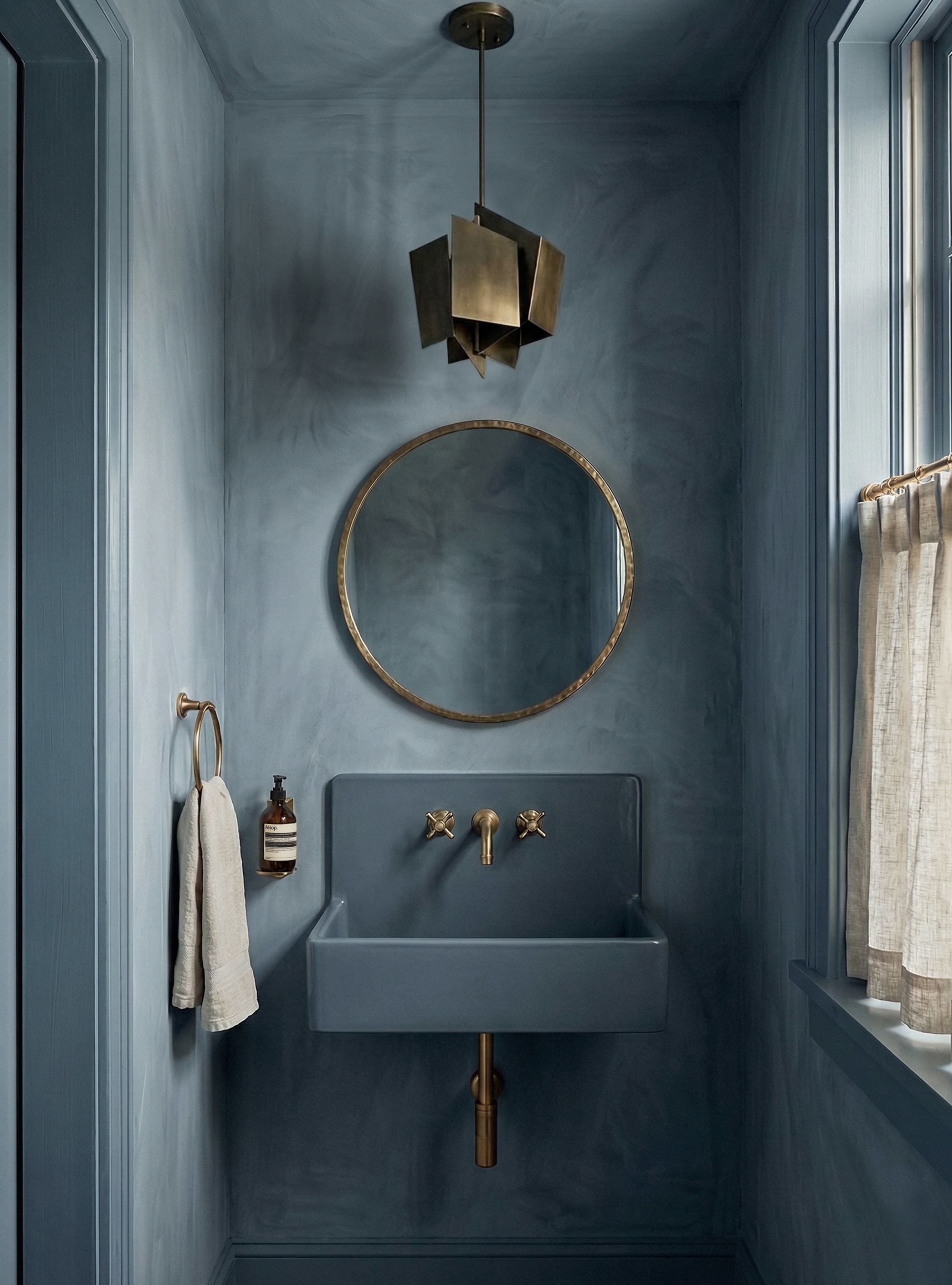 Blue color drenched bathroom with blue limewash paint, vintage brass pendant, round mirror, blue vanity and brass hardware, cafe curtain, and hand towel on loop