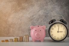Close-up of clock and pink piggy bank with stacked coins.