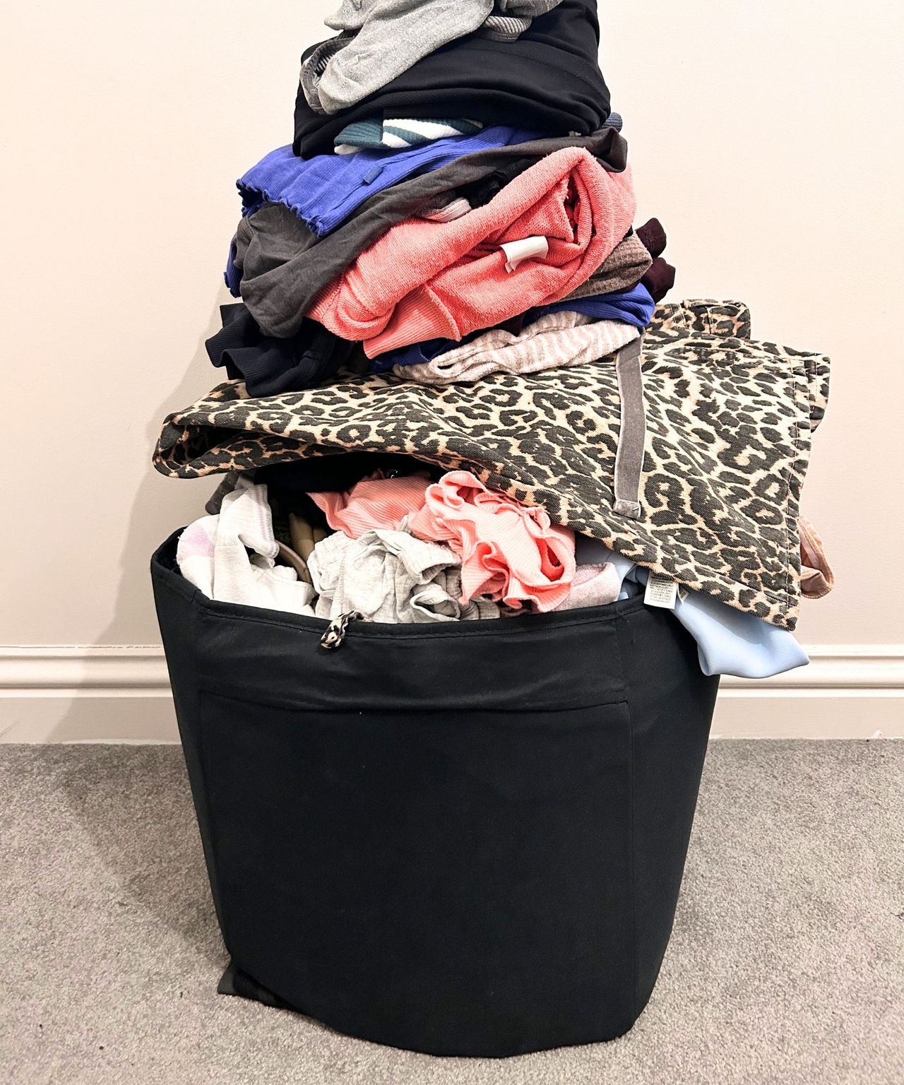 Stack of pink, white, blue, black, grey and leopard print clothing left in a black box on a grey carpet