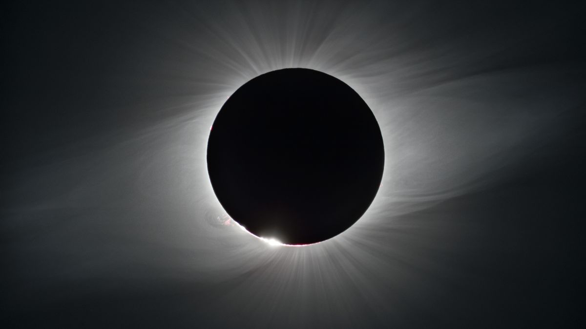 the sun&#039;s face is darkened by the moon during a solar eclipse, showing the wispy lines of the solar outer atmosphere, or corona