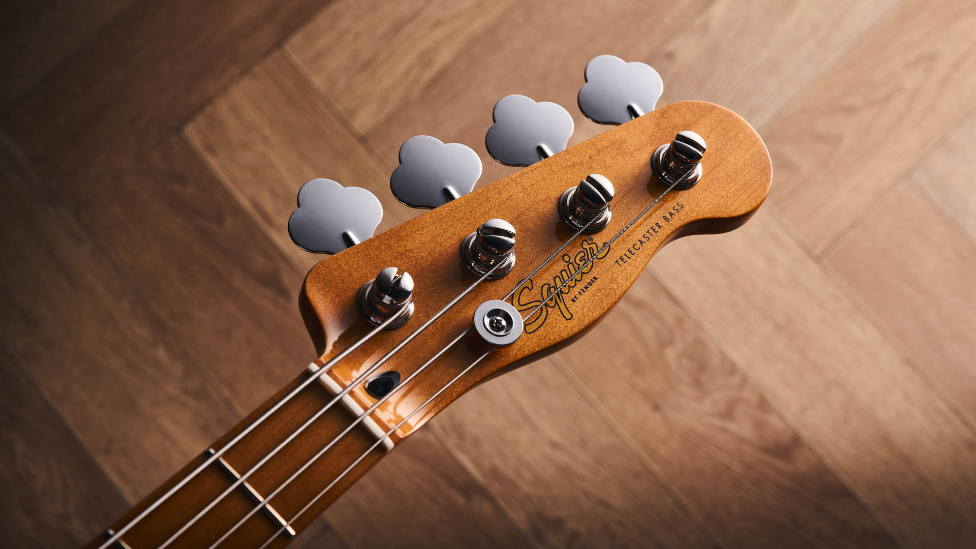 The Squier Classic Vibe Telecaster Bass is a fine-looking four-string in a custard-colored Vintage White, and is here photographed in close-up, against a plain wooden background. It has a single Wide Range humbucker.
