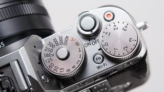 Close-up of silver Fujifilm X-T1 top plate on a white background, showing the ISO and exposure compensation dials as well as the shutter button and on/off switch