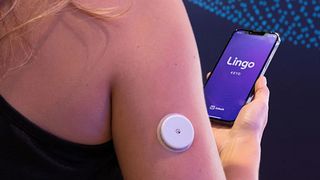 A woman wearing an Abbott sensor on her tricep whilst holding a smartphone with the Lingo app loaded