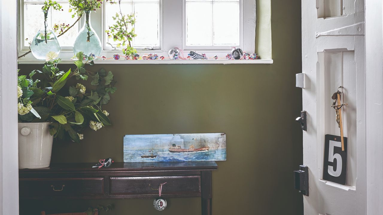 An olive green-painted small hallway with a white front door and a dark wood slim console table