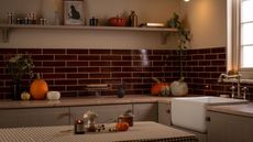 A dimly lit kitchen with deep red subway tile backsplash. Various sized pumpkins scattered on the counters. 