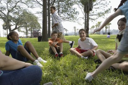 A group of children playing "duck, duck goose" outdoors.