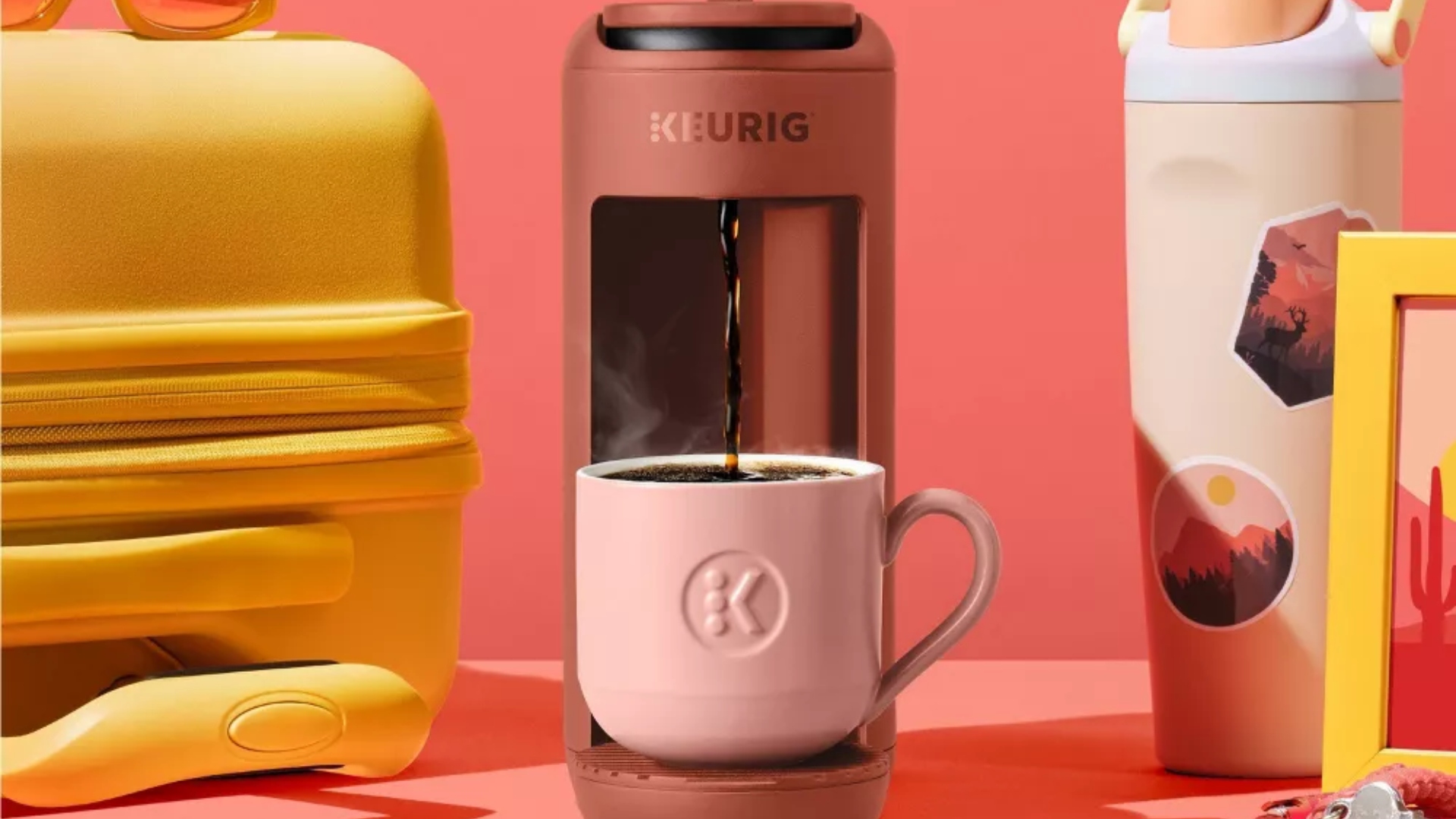 The Keurig K-Mini Mate in Red Rocks with a suitcase and travel mug beside it