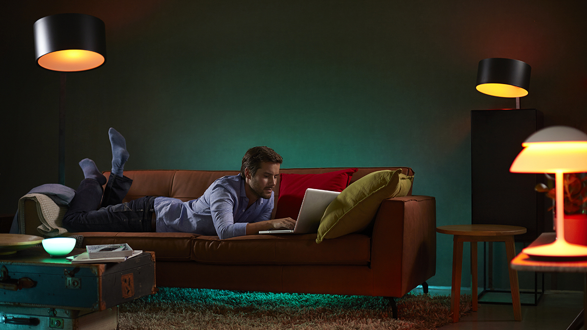 Man lying on sofa using laptop, surrounded by various Philips Hue lights