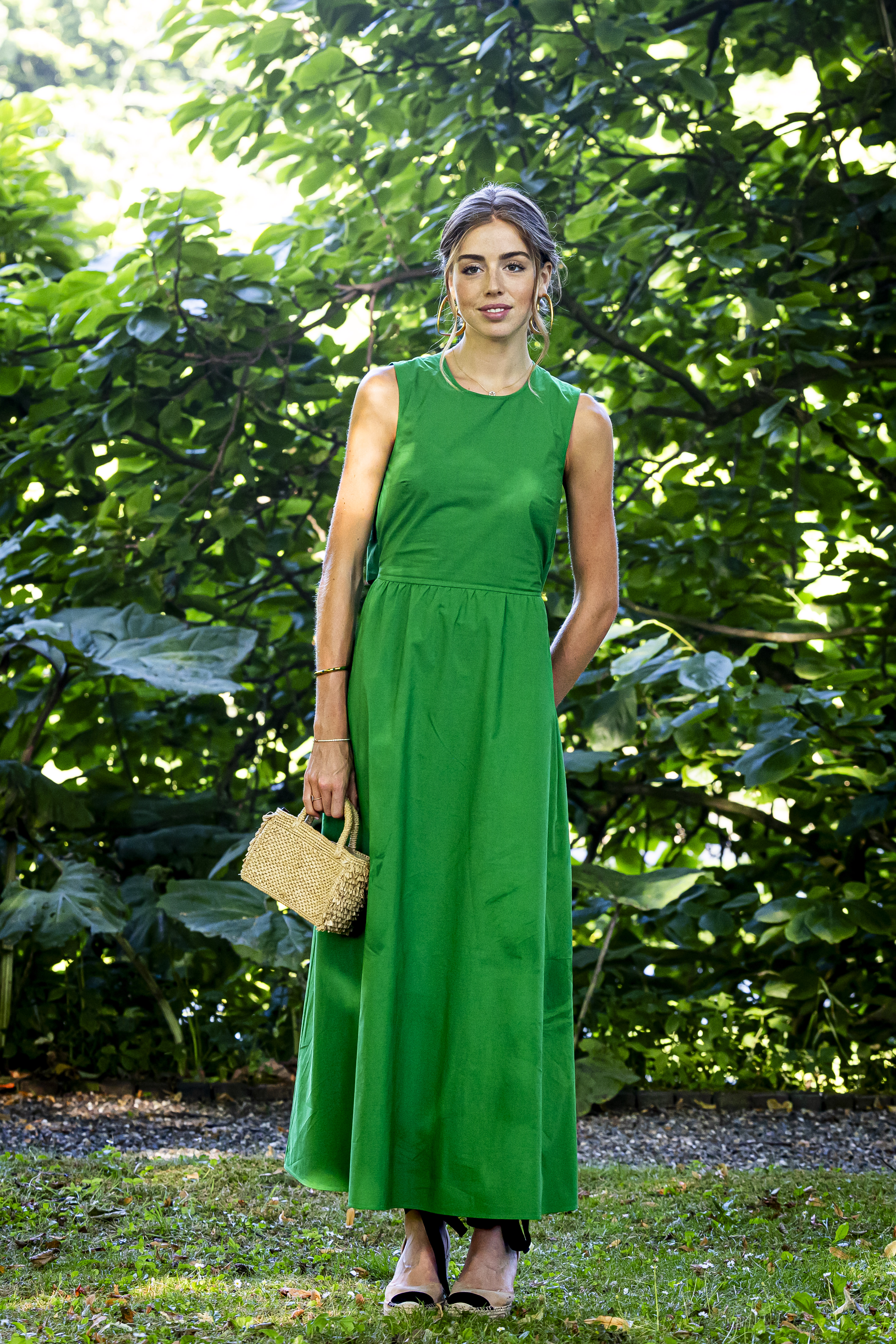 Princess Alexia wearing a long green dress standing in front of a tree and smiling