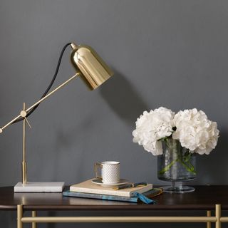 A desk with a vase of hydrangeas and a brass desk lamp