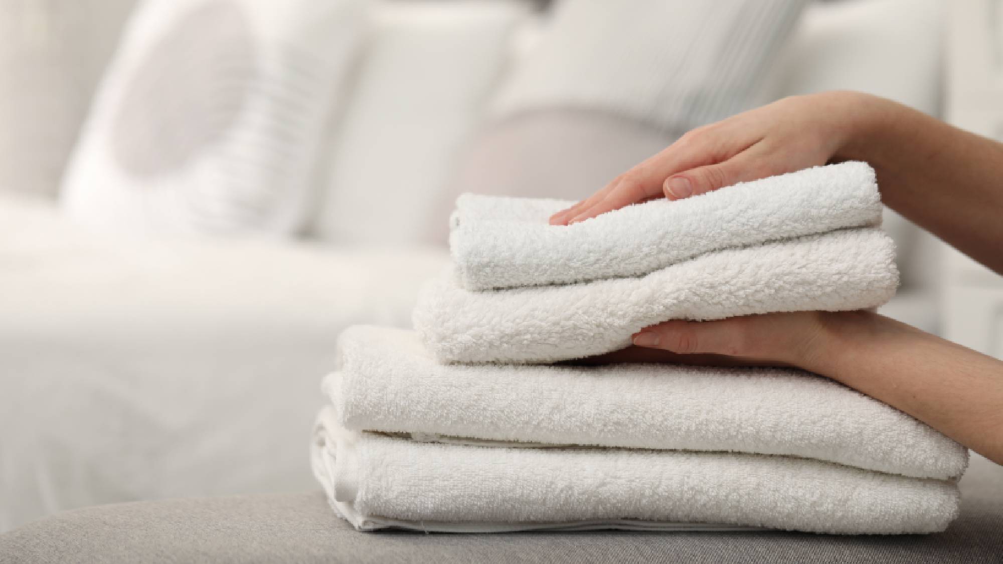 Hands stacking freshly washed, soft white bath towels