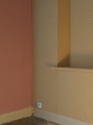 A pink wall next to a brown fabric covered wall with a wooden floor in front of it.