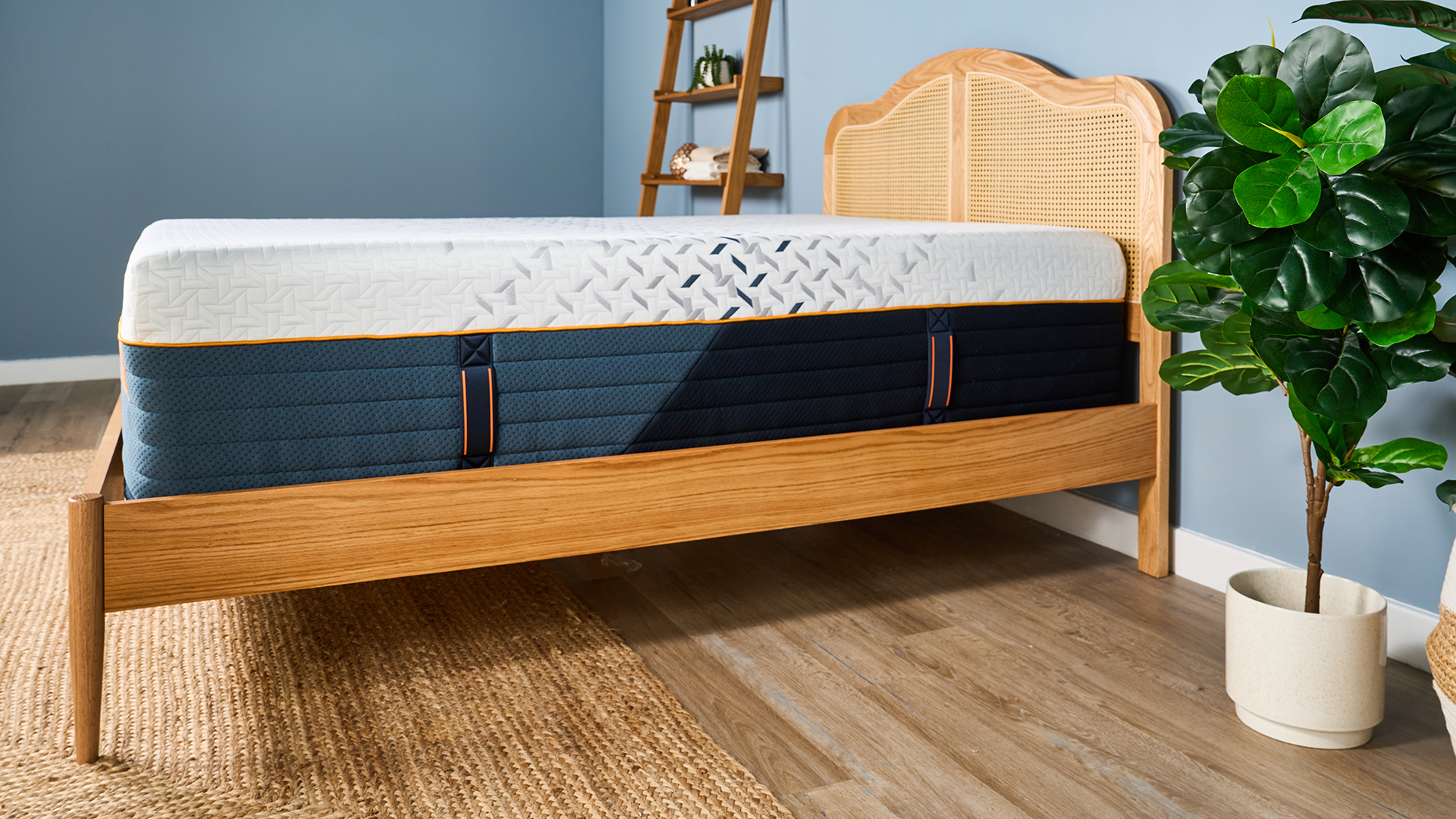 A side on photo of the Nectar Ultra Hybrid mattress on a wooden bed frame, showing the handles sewn on and the orange details