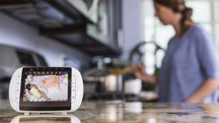 A close-up of a baby monitor on a kitchen counter. It displays the image of a baby sleeping