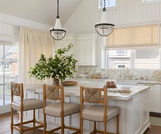 white shaker kitchen with large doors and windows with linen curtains and blinds and rattan bar stools