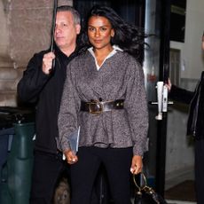 Simone Ashley walks outside in New York wearing black carpi leggings with a tweed belted jacket and mole suede heels.
