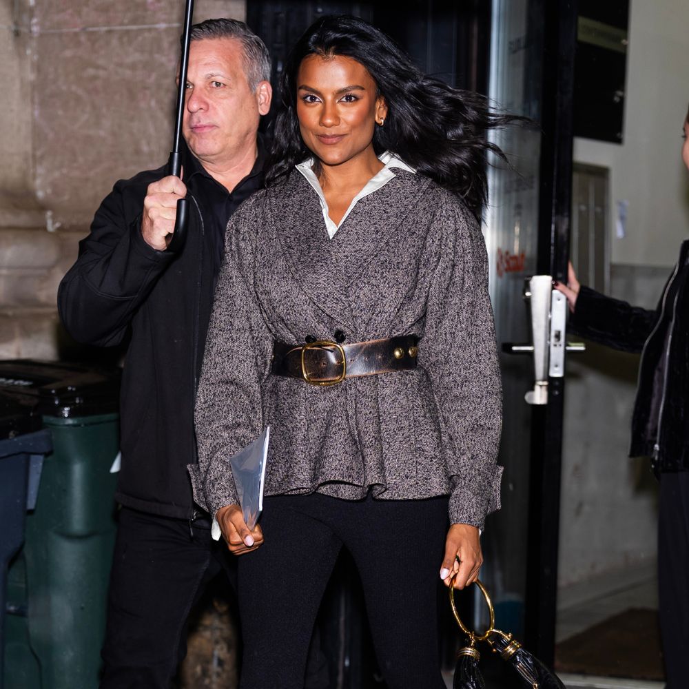 Simone Ashley walks outside in New York wearing black carpi leggings with a tweed belted jacket and mole suede heels.