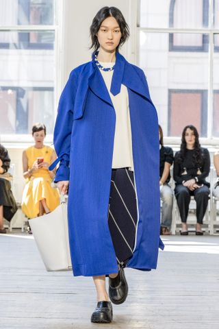 A photo of a model wearing the Proenza Schouler x Sorel Caribou Mule with a cobalt blue trench coat.