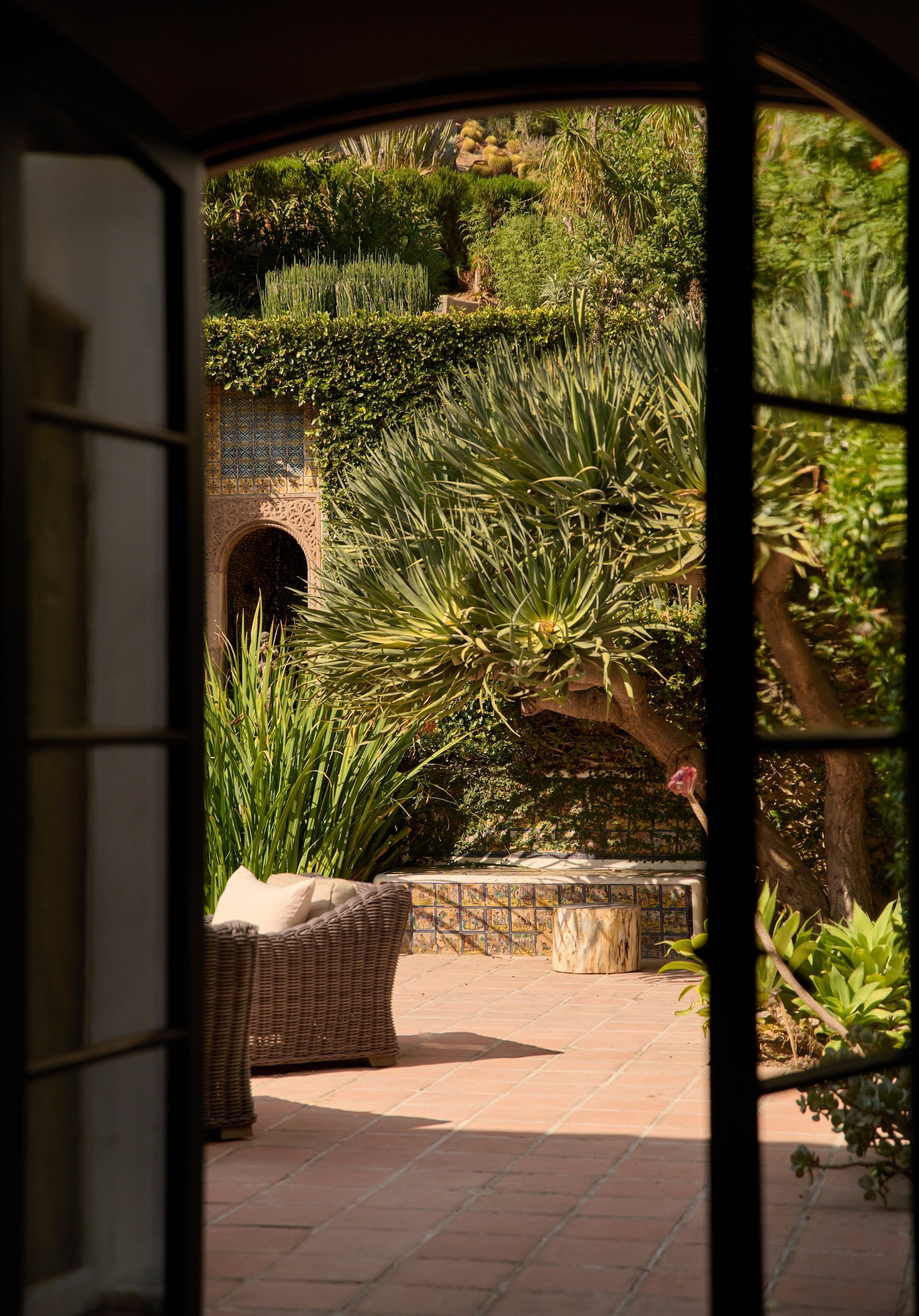 Photo taken of sunny patio area with white chairs and green trees through open doors.