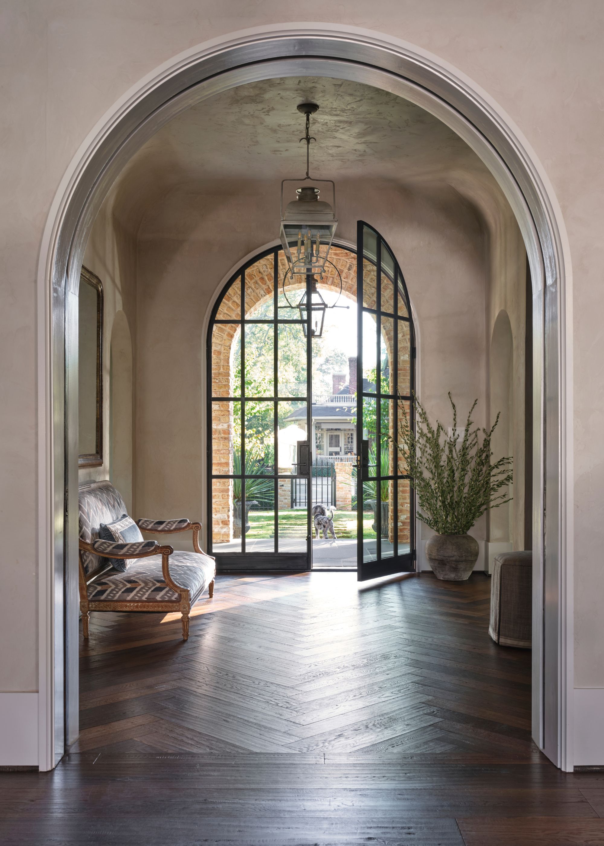 A large entryway with parquet flooring and arched French doors.