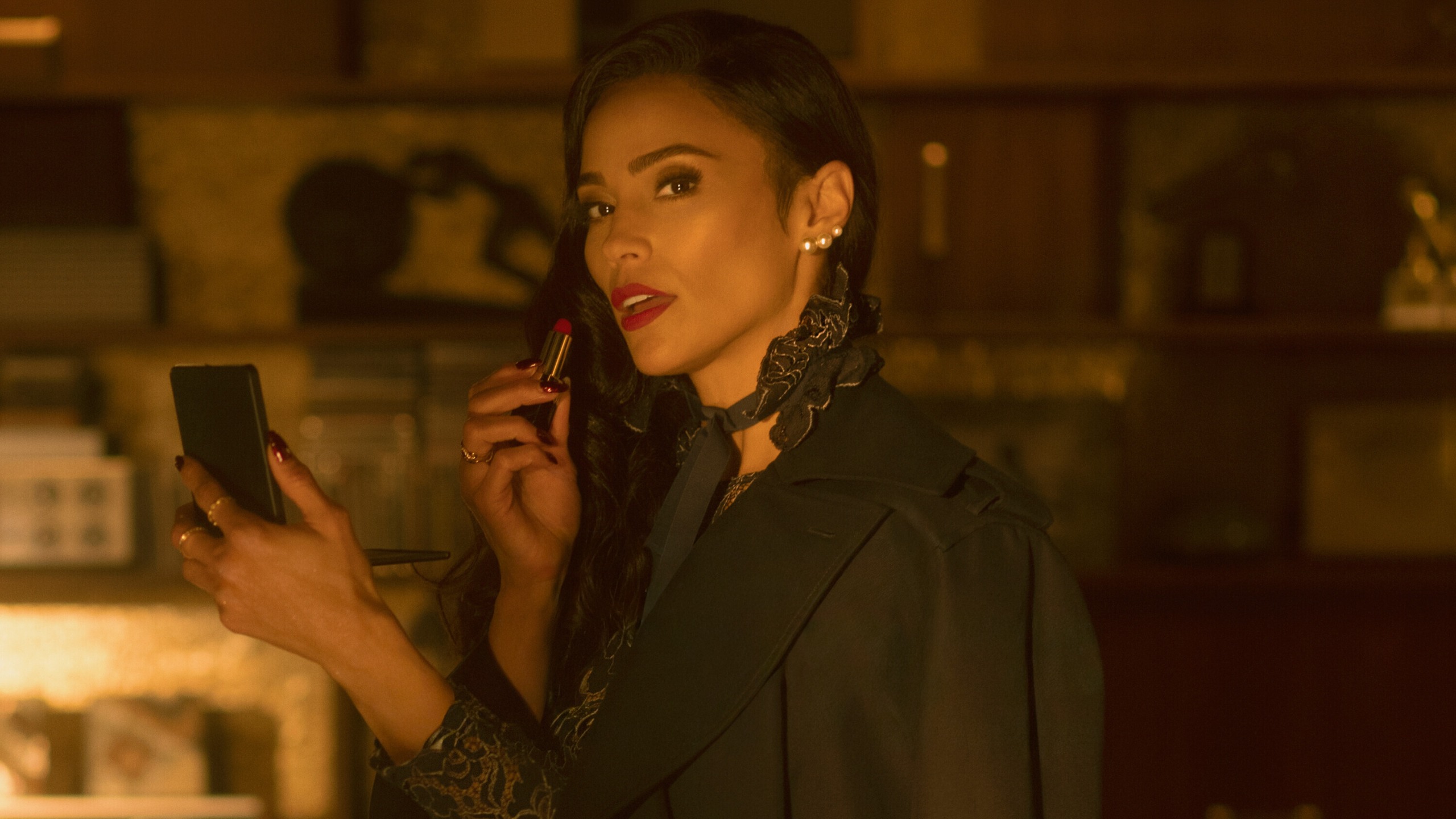 Paula Patton as Daniella Hernandez holding red lipstick and a compact mirror while looking at the camera.