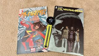 A Garmin watch showing a 5K time, sitting on top of Ms. Marvel and Walking Dead comic books