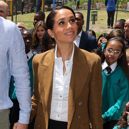 Meghan Markle tours a school wearing a loro piana blazer and a white button down shirt with butterfly earrings previously worn by Princess Diana