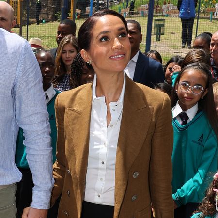 Meghan Markle tours a school wearing a loro piana blazer and a white button down shirt with butterfly earrings previously worn by Princess Diana