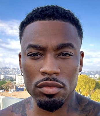 headshot of a black man with tattoos and a mustache