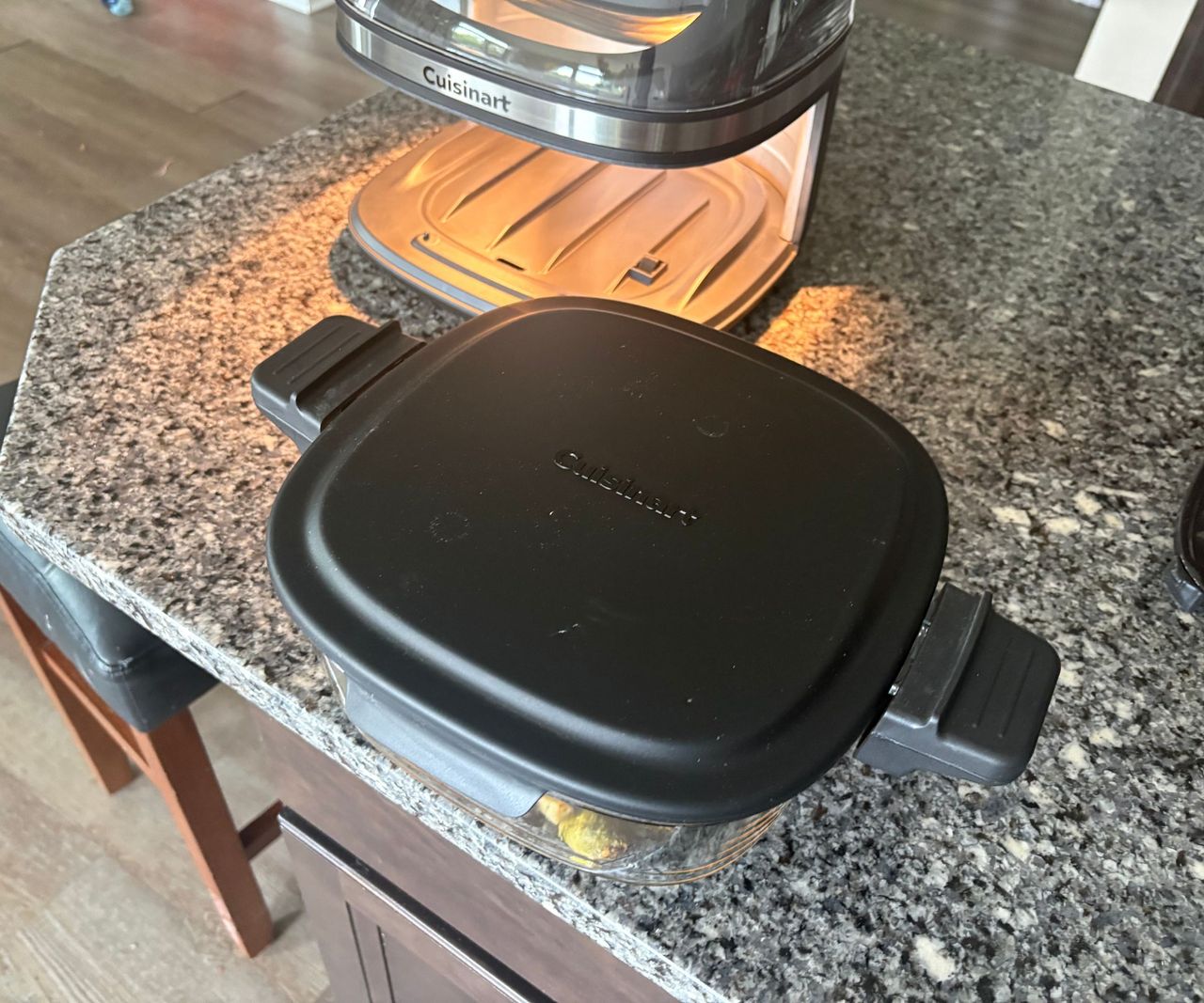 The glass basket of the Cuisinart glass air fryer on a granite countertop with the black lid securely on top.