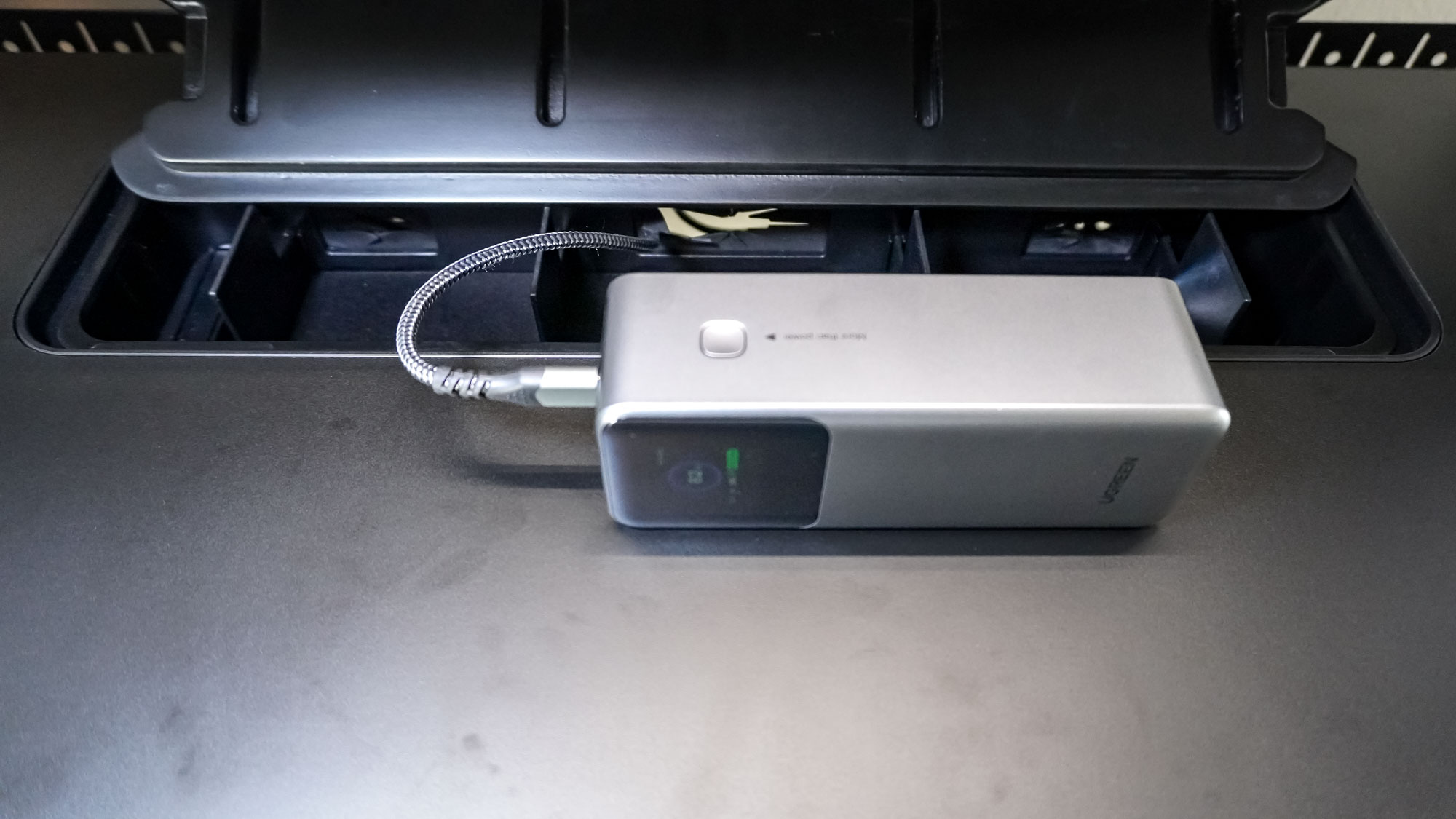 The built-in storage compartment in the Corsair Platform:4 Elevate Desk being used to charge a large portable battery