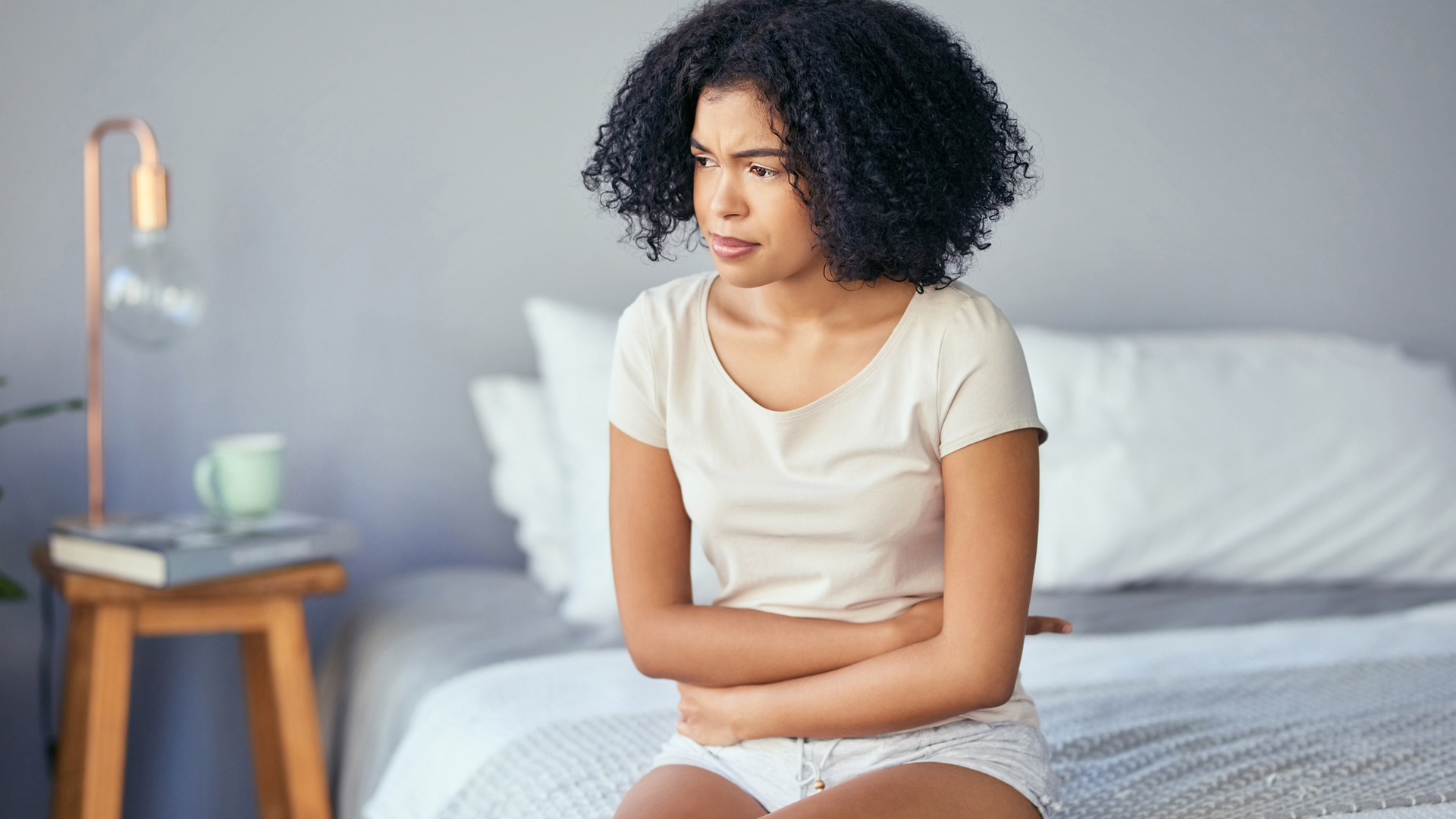 woman holding her stomach sat on her bed