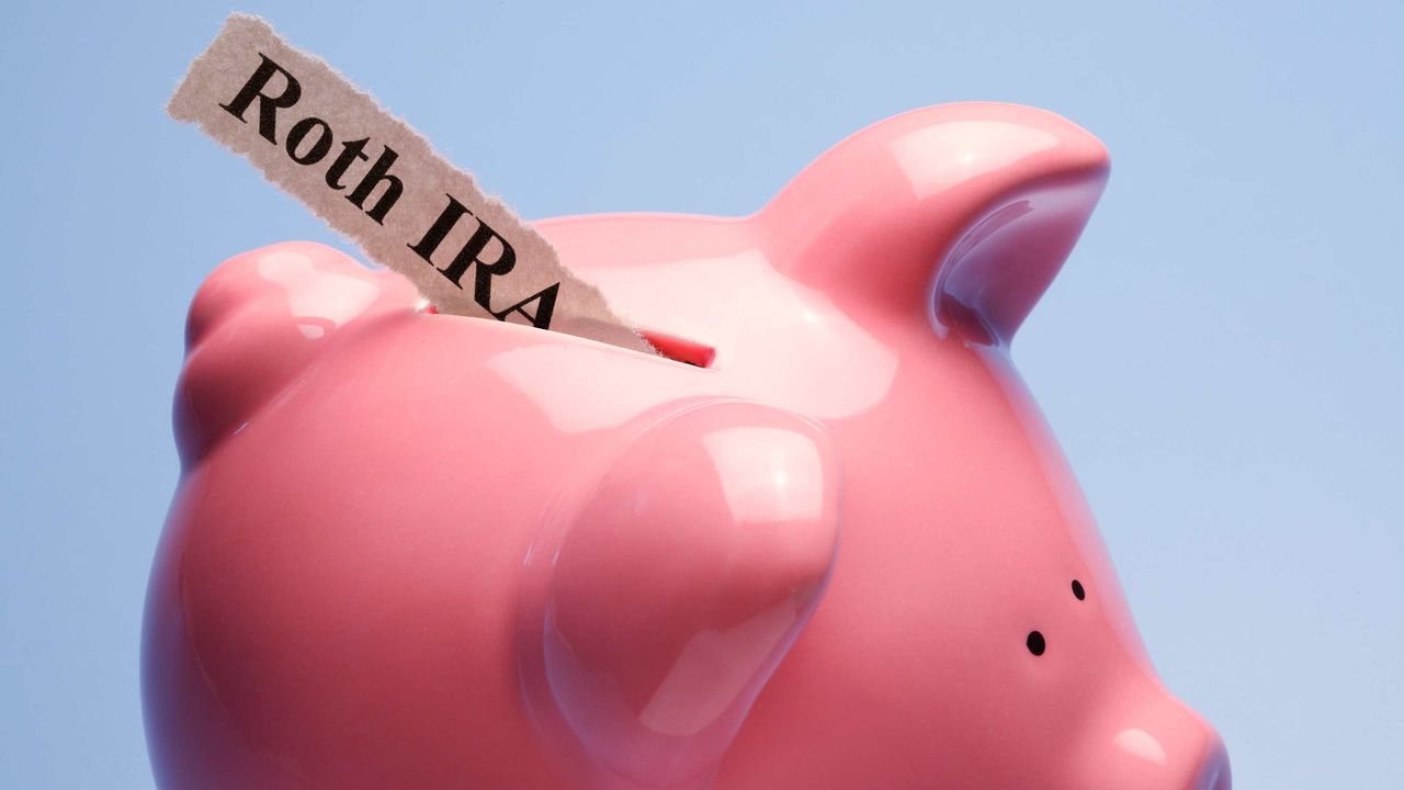 &amp;quot;Roth IRA&amp;quot; is printed on a torn piece of paper that is inserted into the coin slot of a pink piggy bank against a blue background.