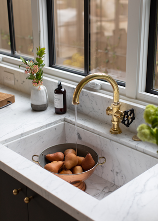 marble sink with a brass tap running over a colander filled with pears