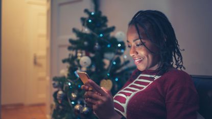 woman lookin at phone next to christmas tree
