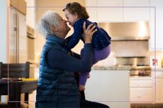 older lady with cropped silver hair lifting a toddler above her head