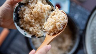 White rice on a wooden spoon held up from a bowl