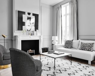A monochromatic black and white living room with modern art above a fireplace, white sofa with patterned cushions and black and white geometric print armchairs.
