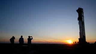 silhouettes of three people at sunset in front of a large rocket on a launch pad in the background