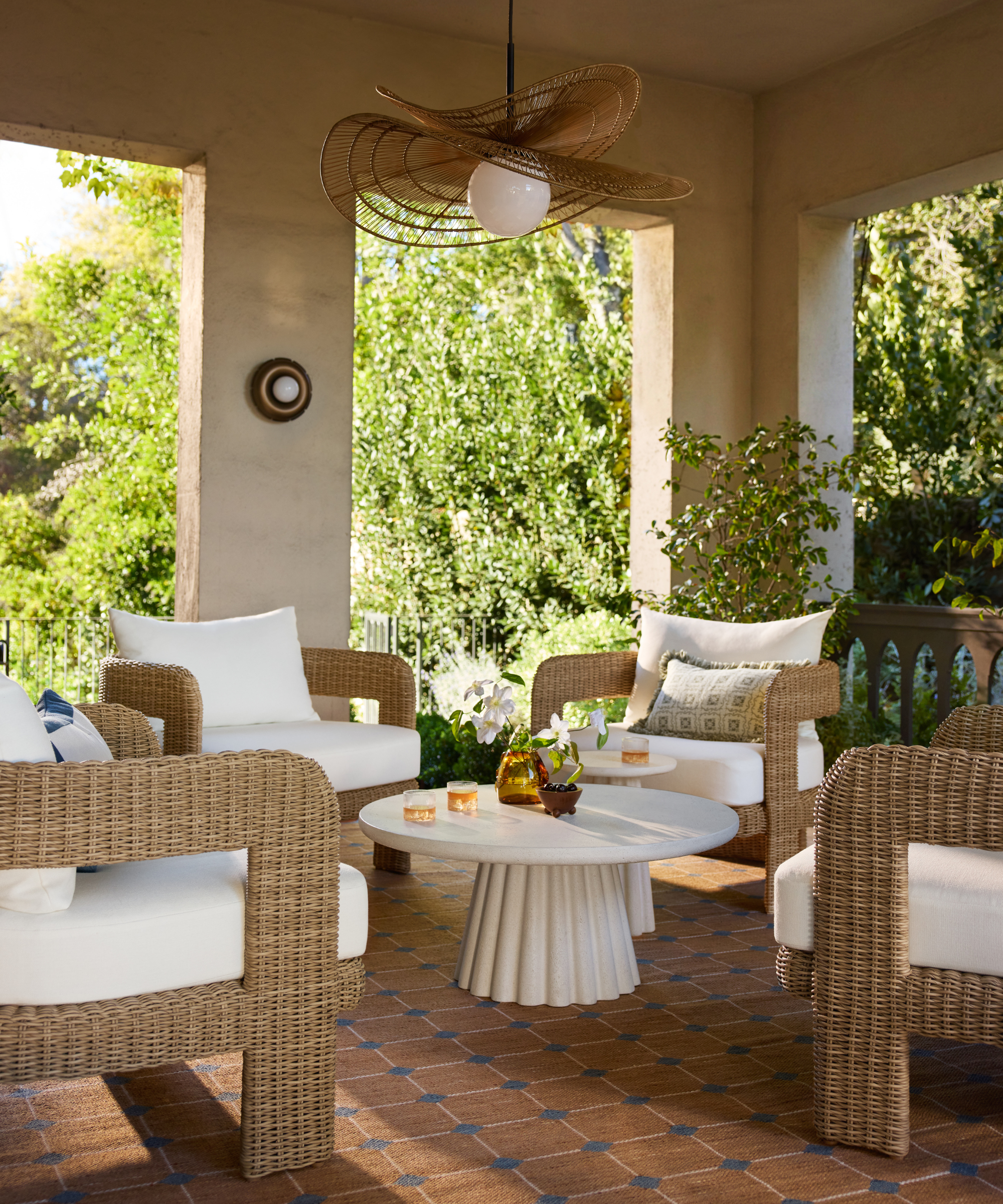 an outdoor living room with four accent chairs, a geometric rug, a coffee table, and an organic-shaped ceiling lamp