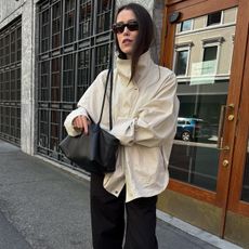 Annabel wears an ivory technical jacket, black bag, and black trousers.
