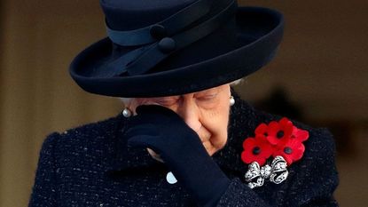 Queen Elizabeth wipes a tear from her eye with her gloved hand.