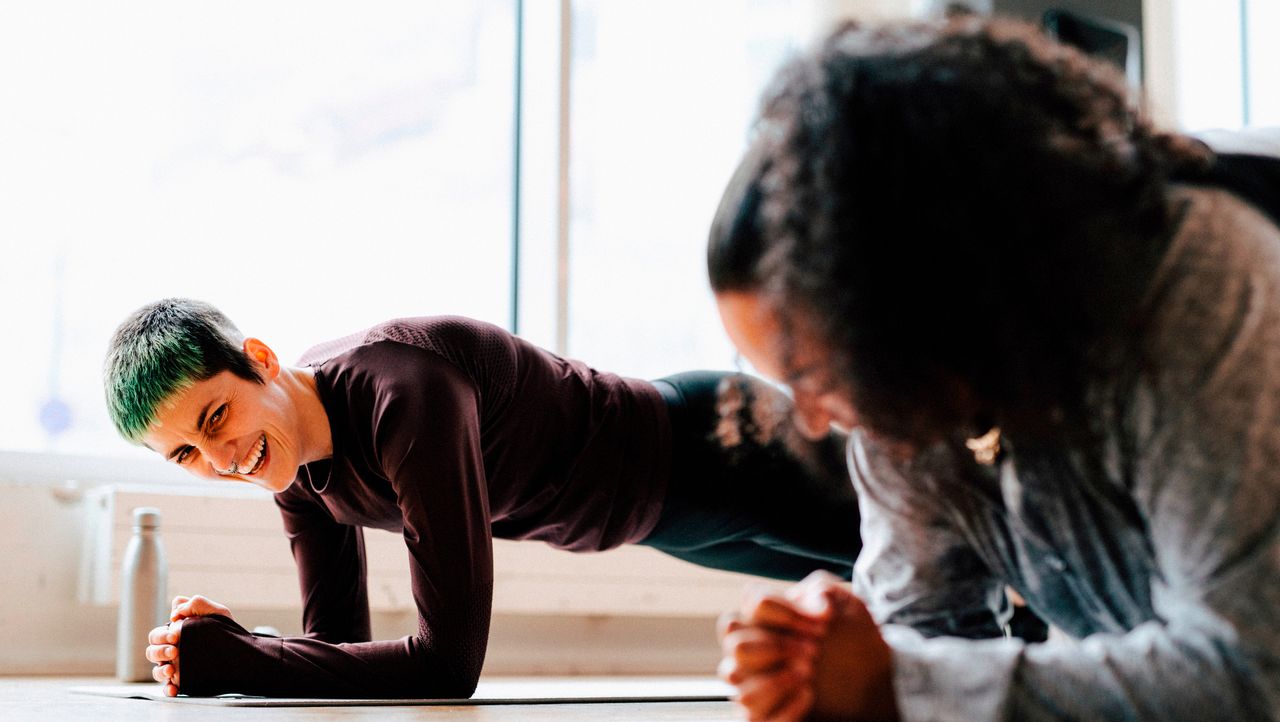 Two women holding plank position in fitness studio. They are both smiling.