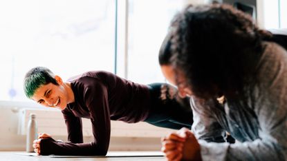 Two women holding plank position in fitness studio. They are both smiling.