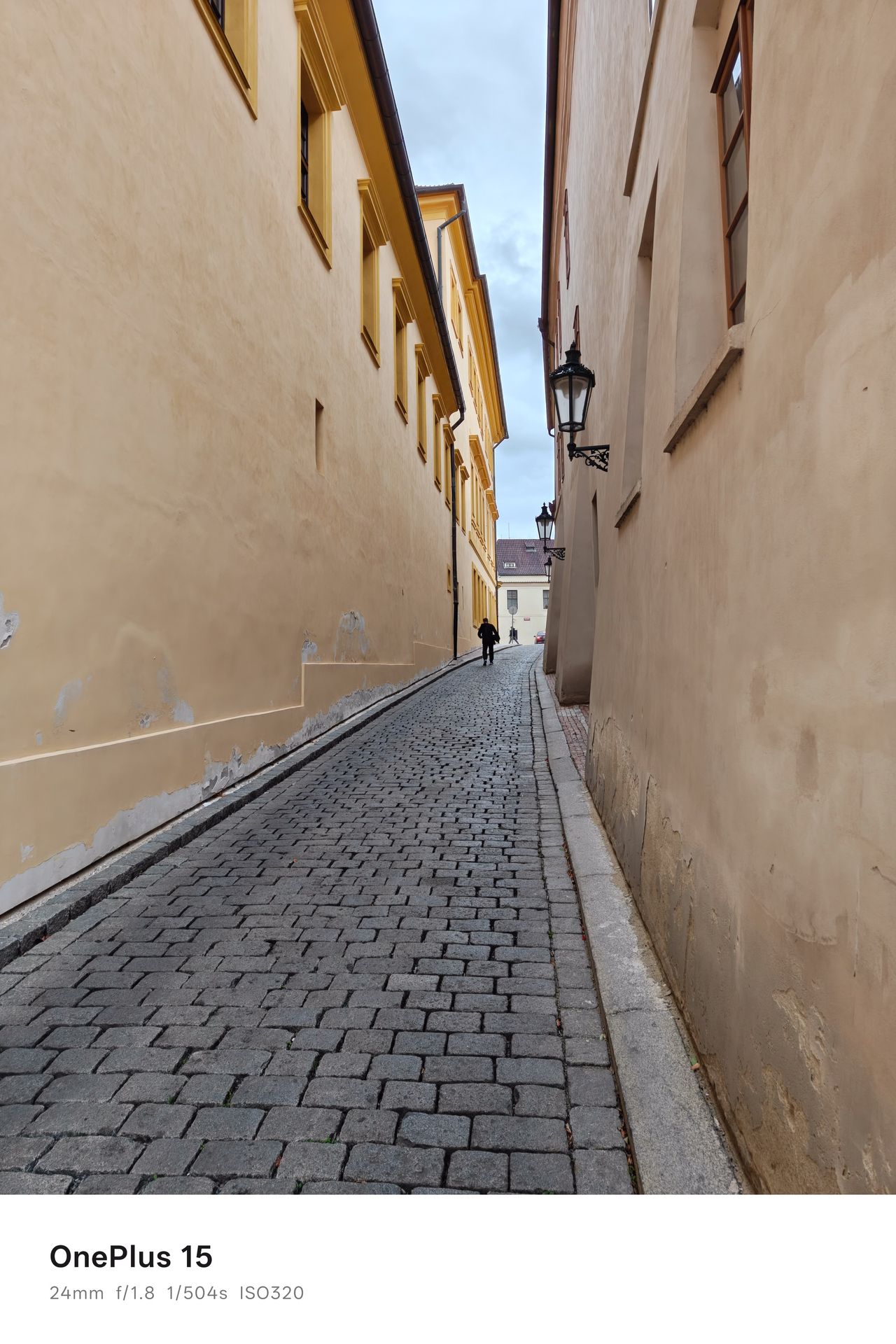 A person walking up a long narrow cobbled path between two building buildings in Prague