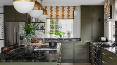 a kitchen with green cabinets with gold hardware, black marble countertops, and gold pendant light fixtures