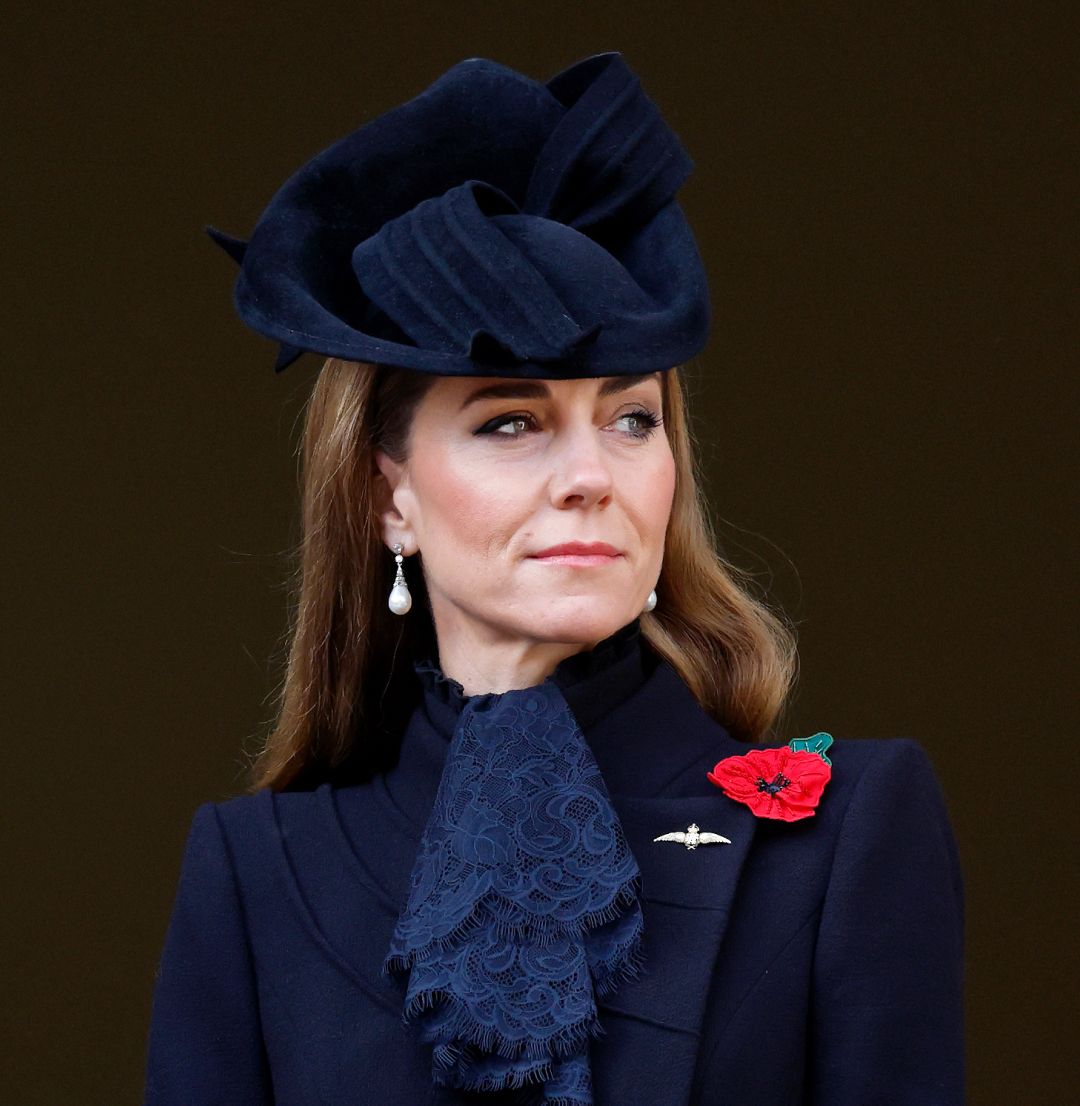 Kate Middleton wearing a black coat and hat with a red poppy pin